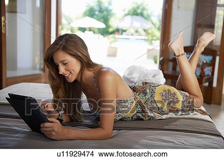 Picture - Woman on bed relaxing with ipad. Fotosearch