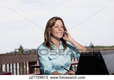 Stock Image - Woman on cell phone with laptop. Fotosearch