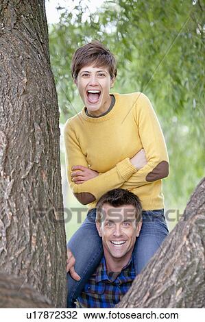 Woman on mans shoulders by a tree View Large Photo Image Stock Image - Woman on mans shoulders by a tree. Fotosearch