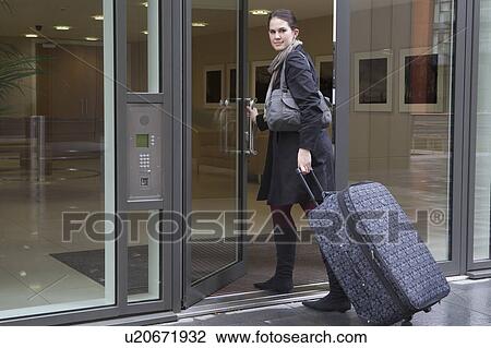 Stock Image - Woman pulling bag through doorway. Fotosearch