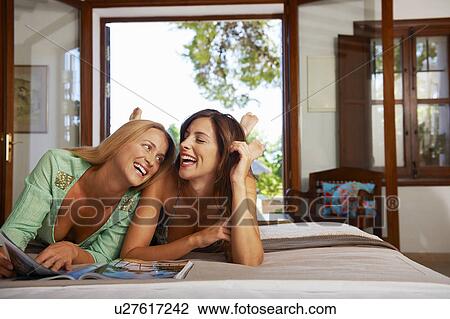 Stock Image - Woman relaxing reading magazine on bed. Fotosearch
