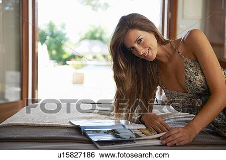 Stock Photograph - Woman relaxing with magazine on bed. Fotosearch