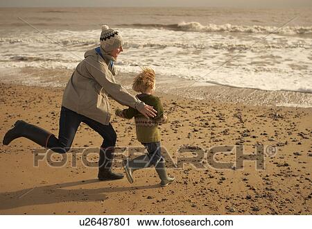 Stock Image - Woman running playing with boy on beach. Fotosearch