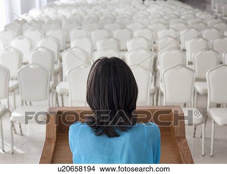 Picture - Woman standing before empty chairs. Fotosearch