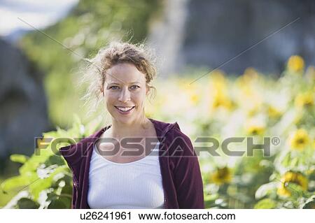 Stock Image - Woman standing between sunflowers. Fotosearch