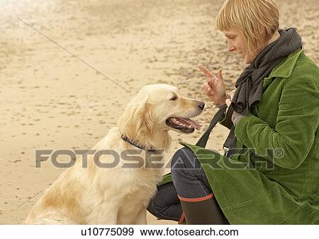 Stock Photo - Woman training dog on beach Autumn Fall. Fotosearch
