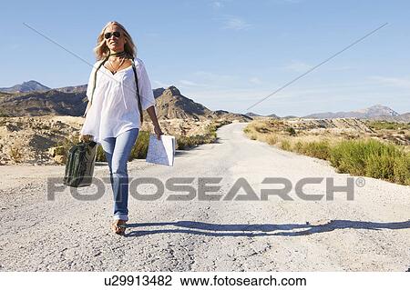Stock Image - Woman walking alone on dusty road. Fotosearch