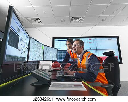 Stock Image - Workers in control room with screens. Fotosearch
