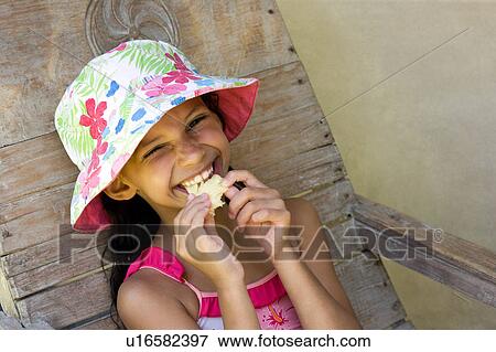 Stock Photo - Youg girl with a hat eating pineapple. Fotosearch
