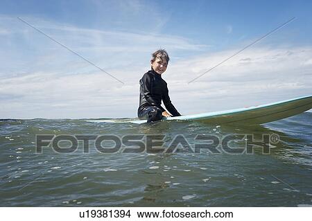 Young boy sitting on surf board at sea View Large Photo Image Picture - Young boy sitting on surf board at sea. Fotosearch