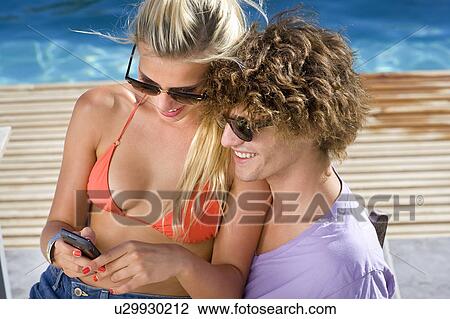 Young couple at poolside look at phone View Large Photo Image Stock Image - Young couple at poolside look at phone. Fotosearch