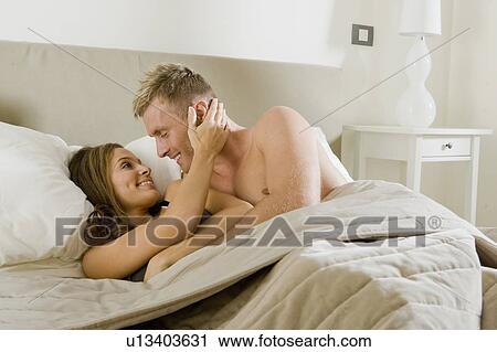 Stock Image - Young couple embracing intimately in bed. Fotosearch