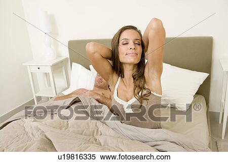 Stock Photography - Young couple in bed, woman stretching. Fotosearch