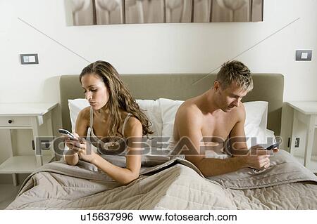 Young couple using smart phones in bed View Large Photo Image Stock Photograph - Young couple using smart phones in bed. Fotosearch
