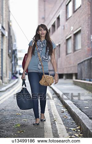 Stock Photograph - Young female walking in street with bags. Fotosearch
