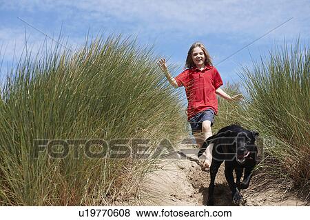 Stock Photo - Young Girl Chasing dog in sand dunes. Fotosearch