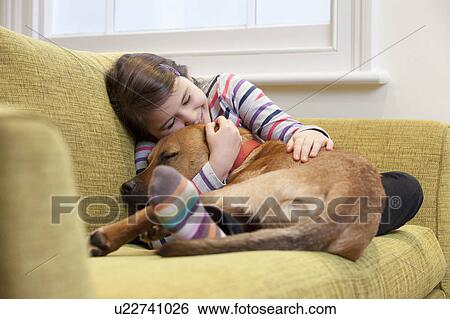 Young girl cuddling her dog on the sofa View Large Photo Image Stock Photograph - Young girl cuddling her dog on the sofa. Fotosearch