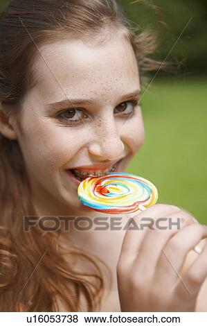 Young girl eating a lollipop in a park View Large Photo Image Stock Photo - Young girl eating a lollipop in a park. Fotosearch