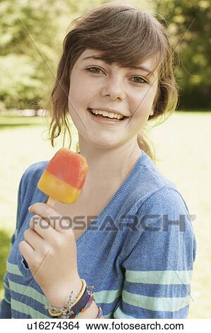 Picture - Young girl eating a popsicle in a park. Fotosearch