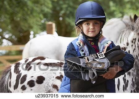 Stock Photography - Young girl holding a saddle with ponies. Fotosearch