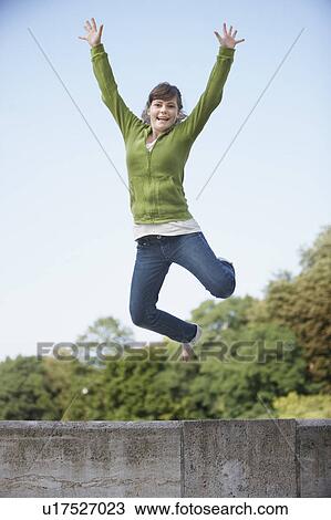 Stock Image - Young girl jumping from stone wall. Fotosearch