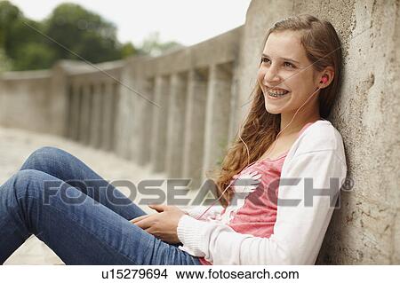 Picture - Young girl sitting listening to ipod. Fotosearch