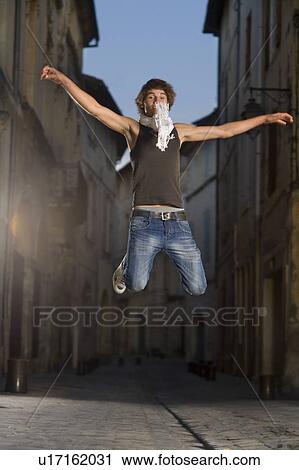 Stock Image - Young man jumps in street at dusk. Fotosearch