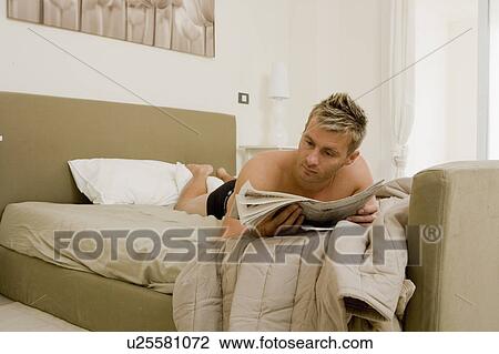 Stock Image - Young man reading newspaper in bed. Fotosearch