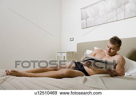 Stock Photo - Young man reading newspaper in bed. Fotosearch