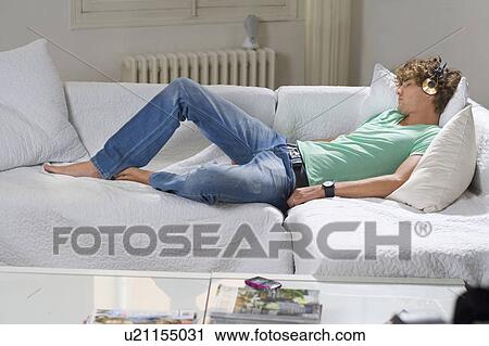 Stock Image - Young man wears headphones relaxes couch. Fotosearch