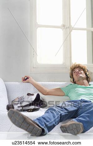 Picture - Young man with headphones lays on couch. Fotosearch