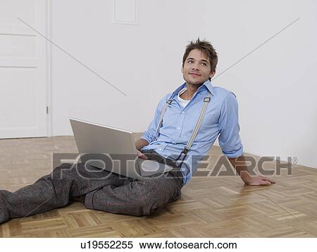 Stock Photography - Young man with laptop in empty flat. Fotosearch