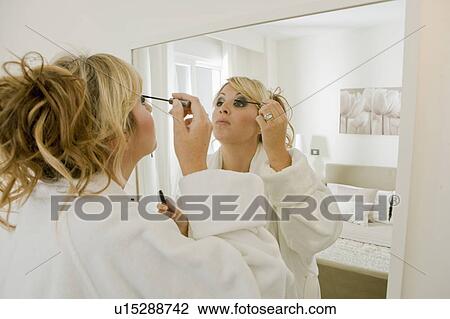 Young woman applying mascara in mirror View Large Photo Image Stock Image - Young woman applying mascara in mirror. Fotosearch