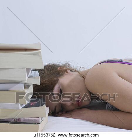 Stock Image - Young woman asleep next to books. Fotosearch