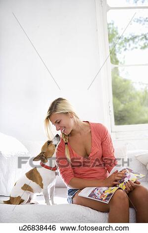 Stock Photograph - Young woman at home with dog on couch. Fotosearch