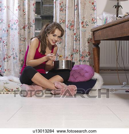 Picture - Young woman eating from cooking pot. Fotosearch