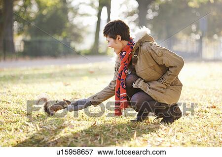 Stock Photo - Young woman feeding a squirrel in a park. Fotosearch