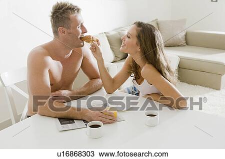 Stock Image - Young woman feeding croissant to man. Fotosearch