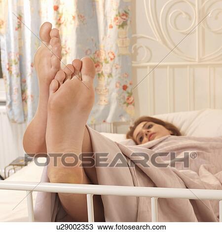 Stock Image - Young woman in bed with feet up. Fotosearch