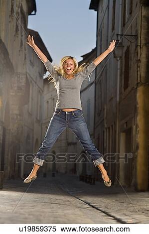 Stock Photography - Young woman jumps in street at dusk. Fotosearch