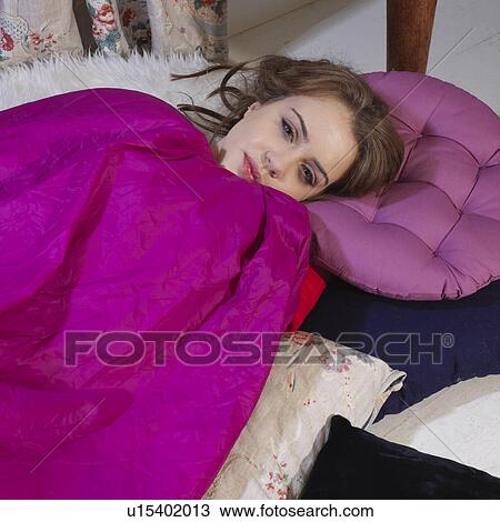 Stock Image - Young woman lying on cushions smiling. Fotosearch