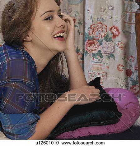 Stock Image - Young woman on cushion laughing. Fotosearch