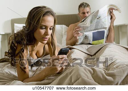 Stock Photo - Young woman using smart phone on bed. Fotosearch