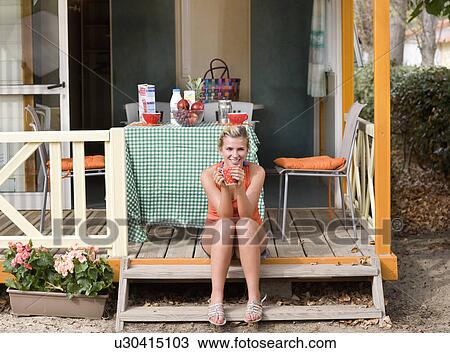 Stock Image - Young woman with coffee sits on steps. Fotosearch