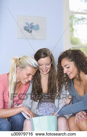 Stock Photograph - Young women look in shopping bag at home. Fotosearch