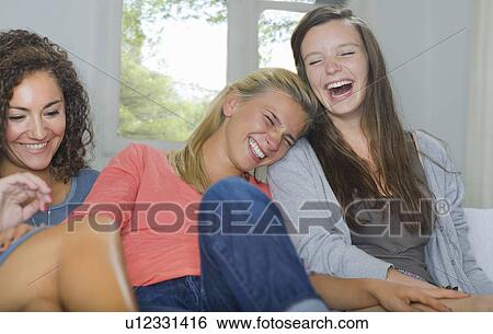 Young women share a laugh sit on couch View Large Photo Image Stock Photograph - Young women share a laugh sit on couch. Fotosearch