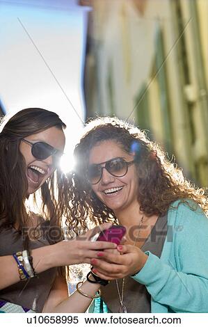 Young women share cell phone in street View Large Photo Image Stock Photography - Young women share cell phone in street. Fotosearch