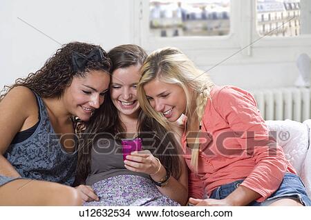 Young women share phone text on couch View Large Photo Image Picture - Young women share phone text on couch. Fotosearch