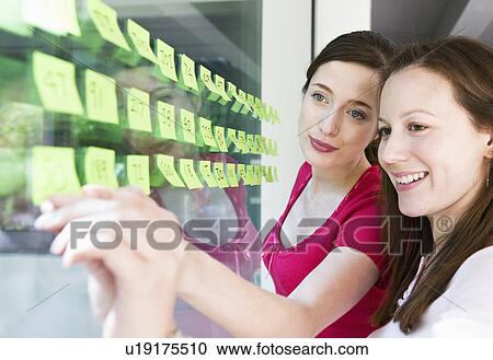 Stock Image - 2 women work with yellow labels. Fotosearch