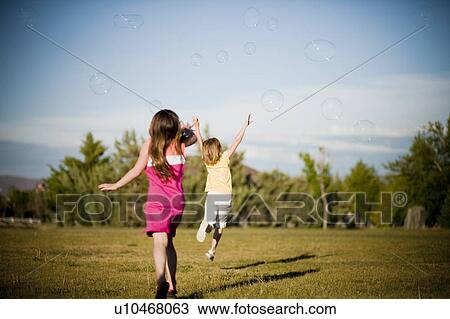 Stock Image - 2 young girls chasing bubbles in park. Fotosearch